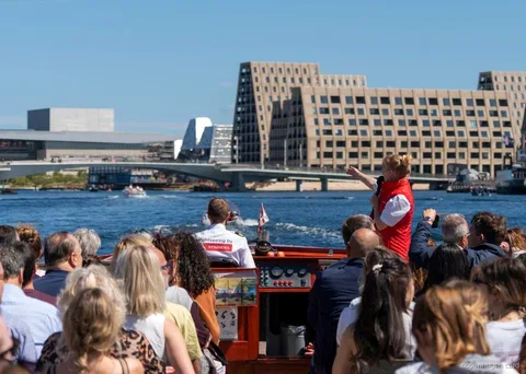 Guia narrando a rota do cruzeiro pelos canais de Copenhague perto da estátua da Pequena Sereia